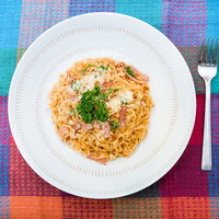 白い丸皿にベーコンとパセリと粉チーズを載せた汁なしチキンラーメンの写真
