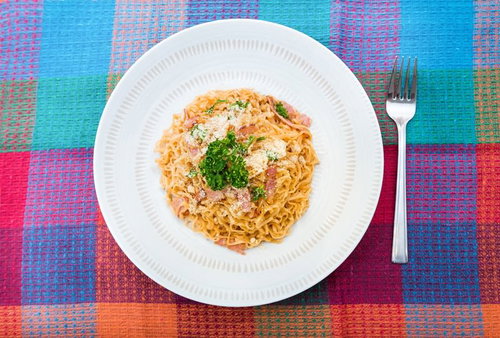 白い丸皿にベーコンとパセリと粉チーズを載せた汁なしチキンラーメン