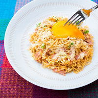 フォークで黄身を持ち上げる粉チーズとベーコンの汁なしラーメンの写真