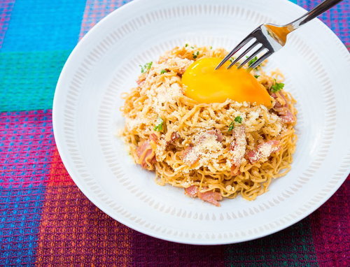 フォークで黄身を持ち上げる粉チーズとベーコンの汁なしラーメン