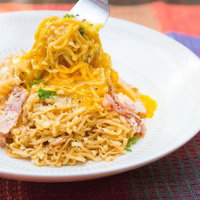 フォークで麺を持ち上げるベーコンと粉チーズの汁なしラーメンの写真