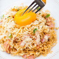 卵黄をフォークで割る途中のカルボナーラ風インスタントラーメンの写真