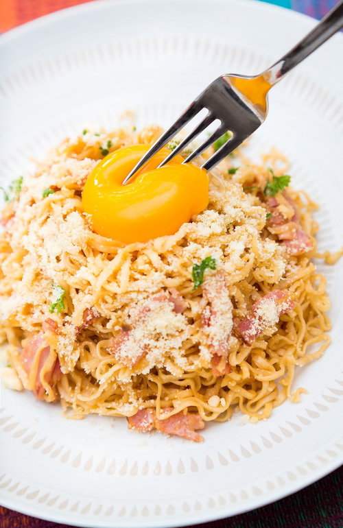 卵黄をフォークで割る途中のカルボナーラ風インスタントラーメン