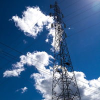 青空を背景に電線を支える鉄塔がそびえるインフラ風景の写真