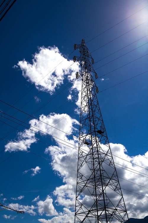 青空を背景に電線を支える鉄塔がそびえるインフラ風景