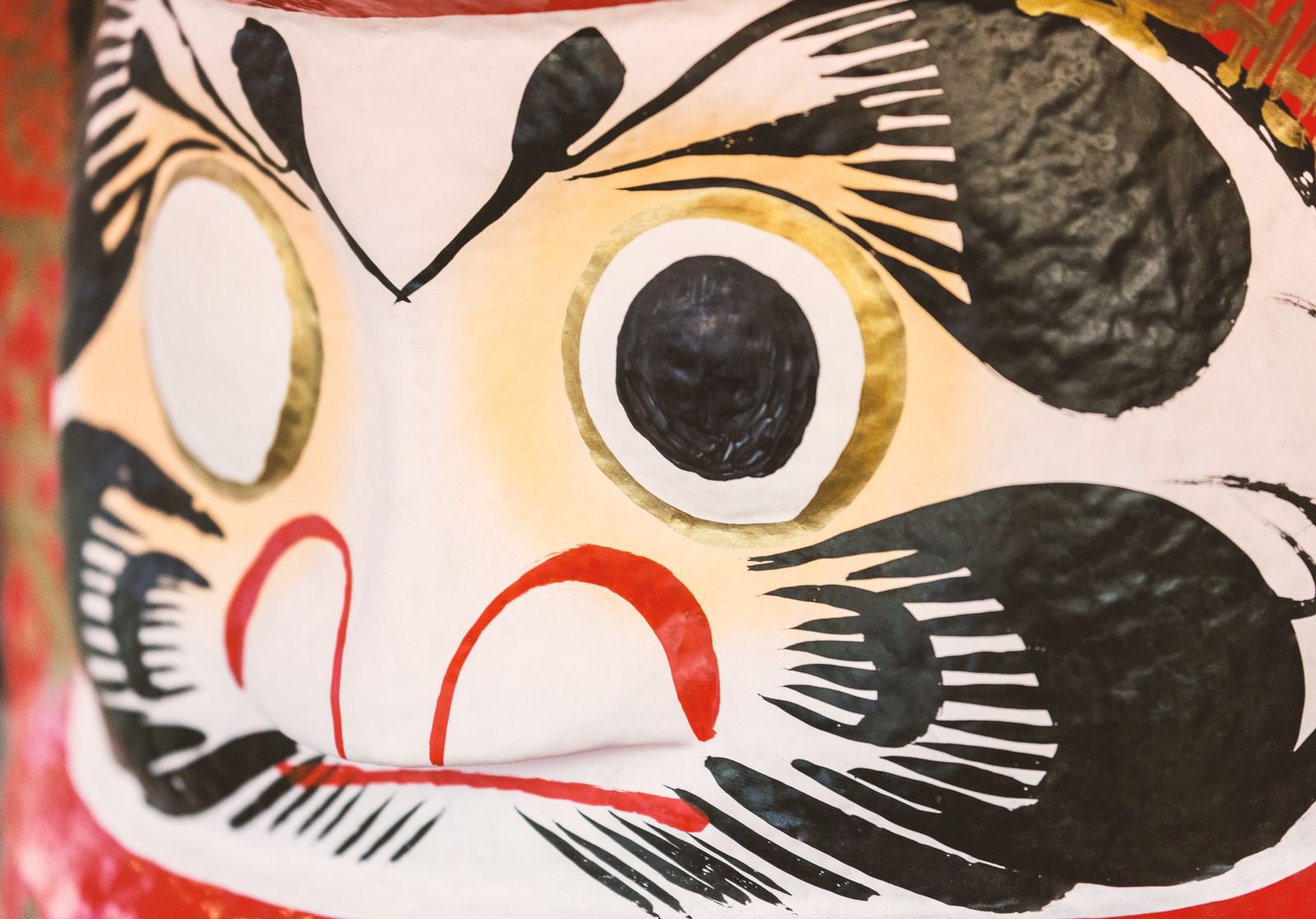 白い紙に描かれた金色の輪と赤い鼻が特徴的な達磨の顔のイラスト