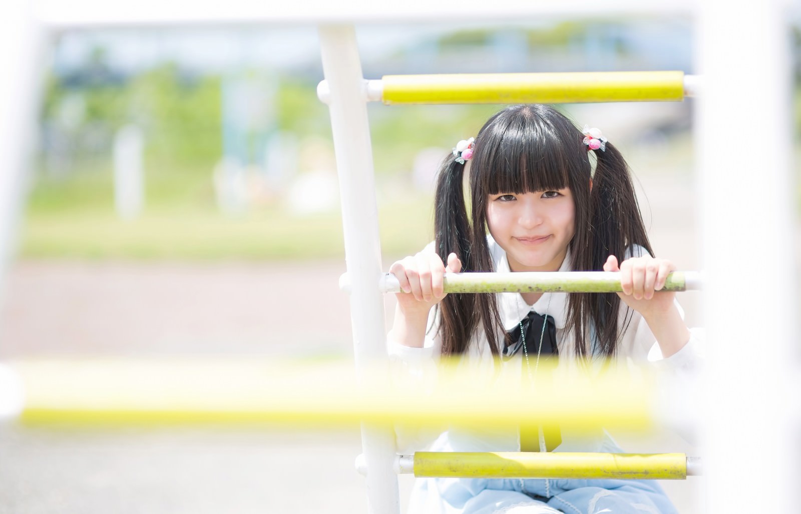遊具の枠から顔を出すツインテールの女の子［モデル：こころ］