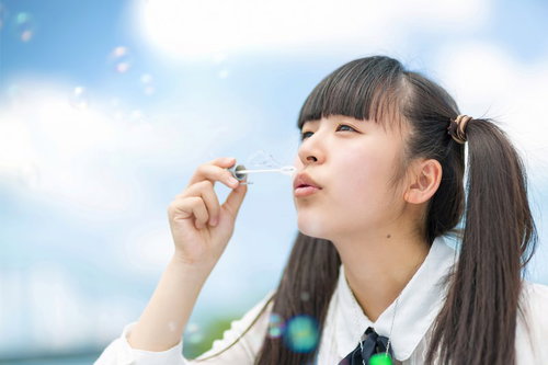 青空に向かってシャボン玉を吹く女の子