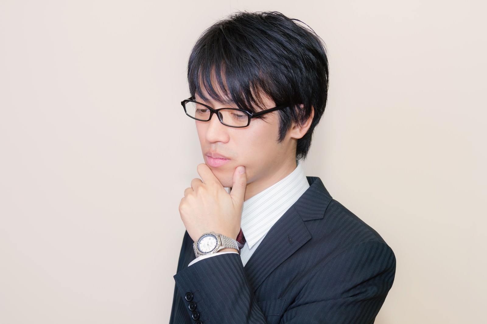 メガネをかけて考え込むスーツ姿の男性［モデル：Tsuyoshi.］