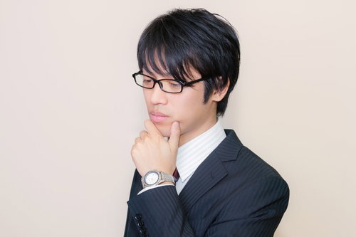 メガネをかけて考え込むスーツ姿の男性