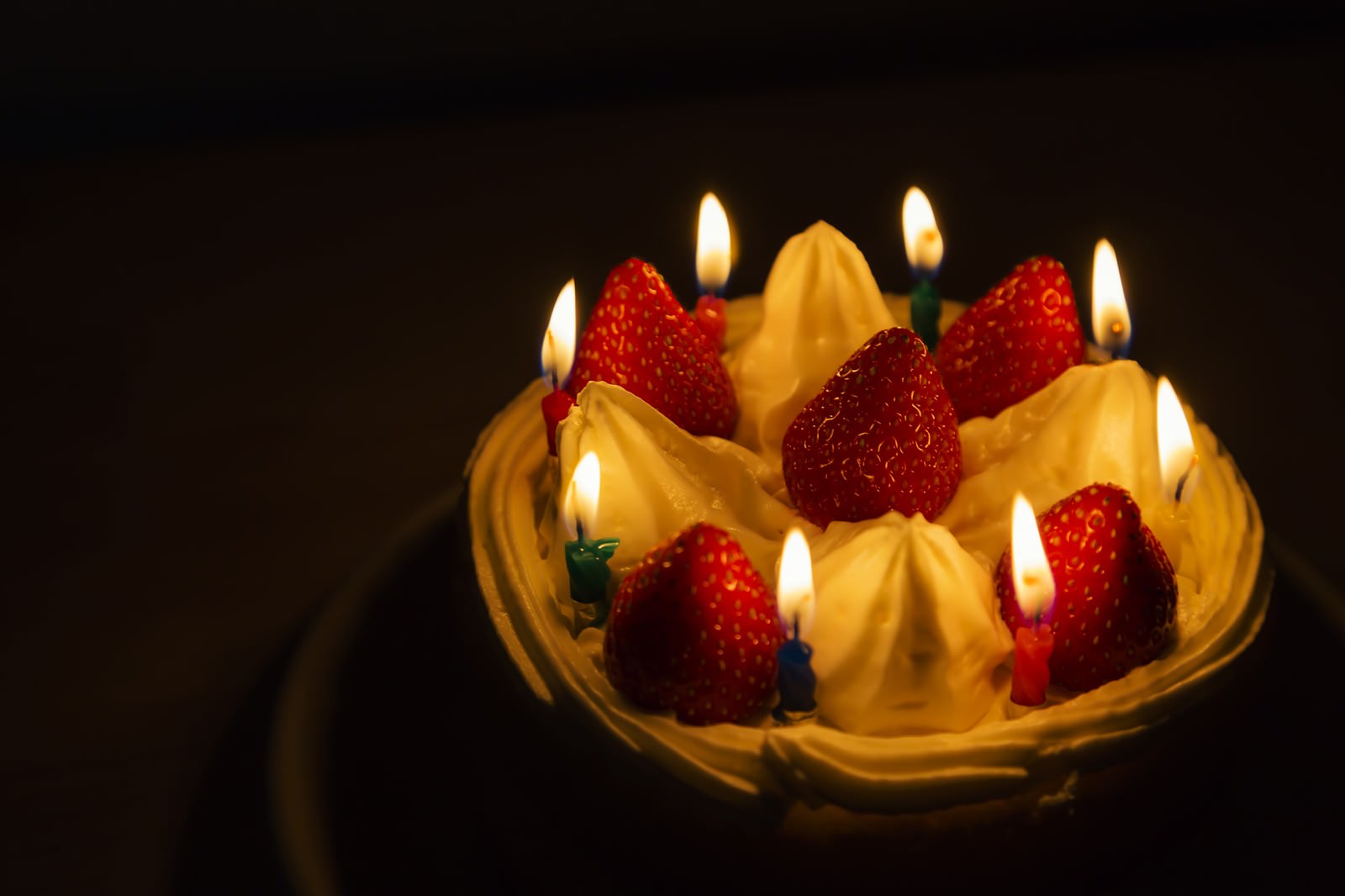 暗い中でろうそくの火が灯るイチゴの誕生日ケーキ