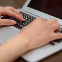 ノートパソコンのキーボードを打つ両手の写真
