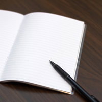 木のテーブルに置かれた見開きのノートとペンの写真