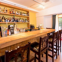 窓から光が差すバーカウンター席と酒瓶棚の写真