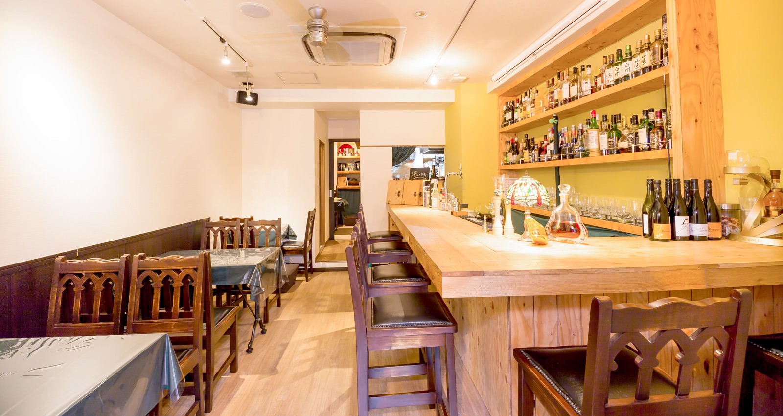 木製カウンターと椅子が並び奥の棚に多数の酒瓶がある料理店の店内