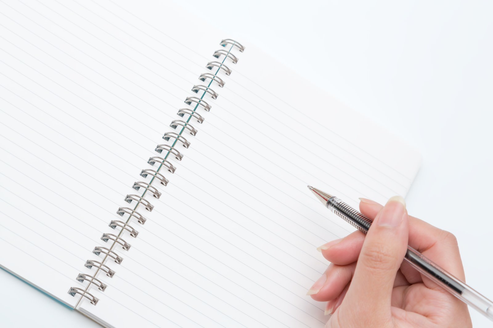 白い机の上で開いたリングノートに右手でペンを構えている俯瞰写真