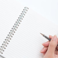 白いリングノートにペンを構える手元の俯瞰の写真