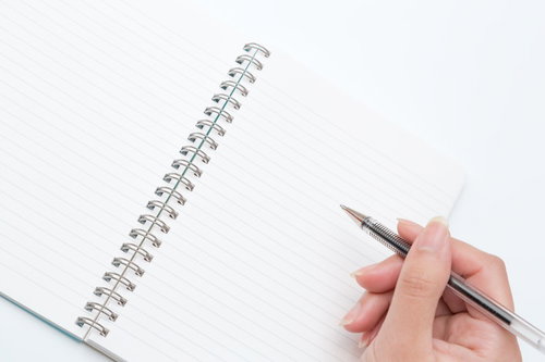 白いリングノートにペンを構える手元の俯瞰