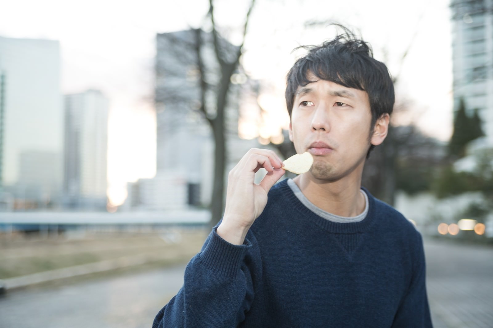 公園でポテチを食べながら考える男性［モデル：大川竜弥］