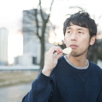 ダイエットは明日からと言いながらポテチを食べる男性の写真