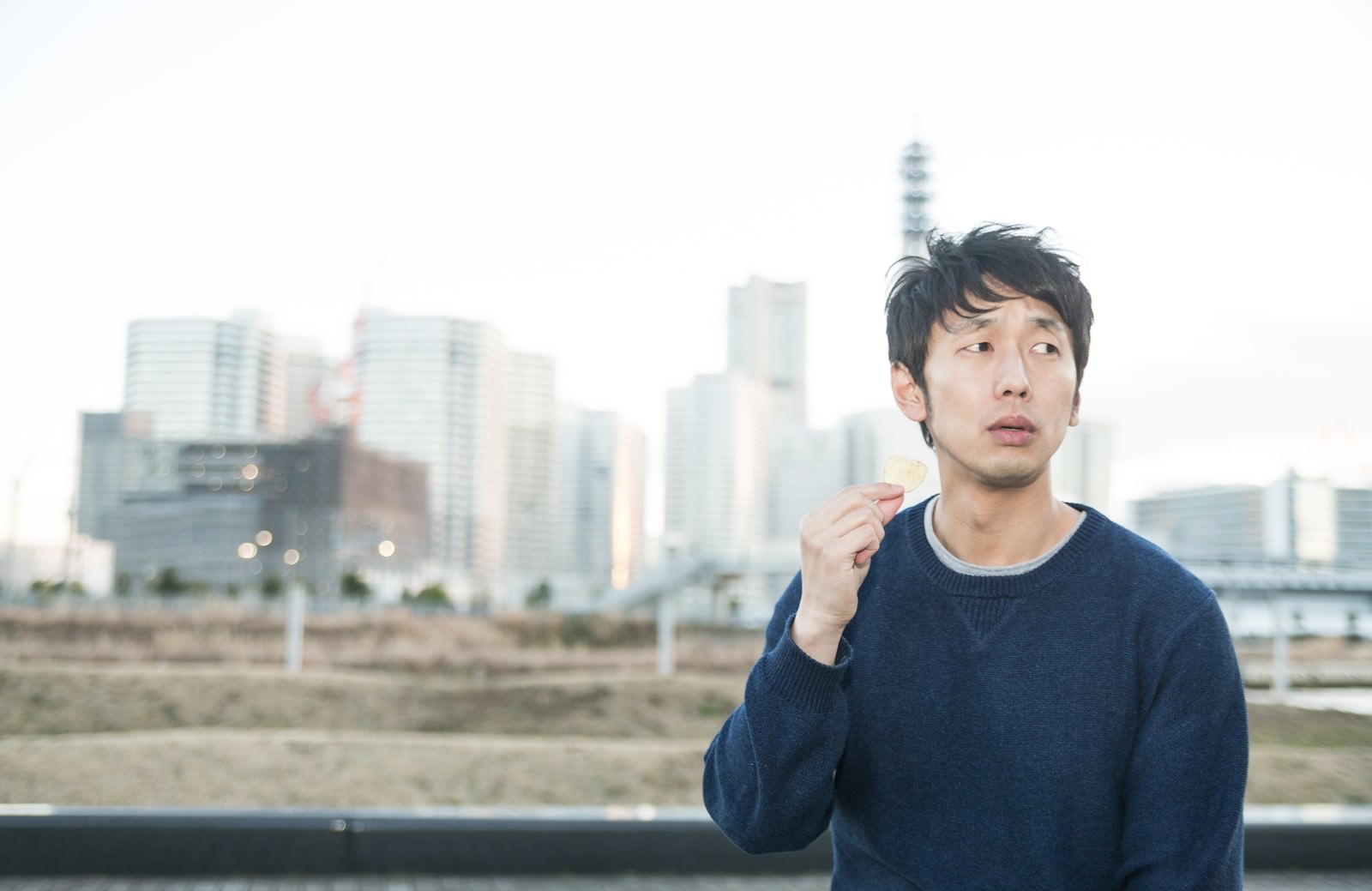 都会の空き地でポテトチップスを食べたそうに見つめる男性［モデル：大川竜弥］