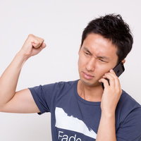 スマートフォンで電話しながら拳を上げる男性の写真