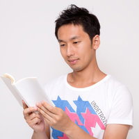 本を開いて読書する白Tシャツの男性の写真