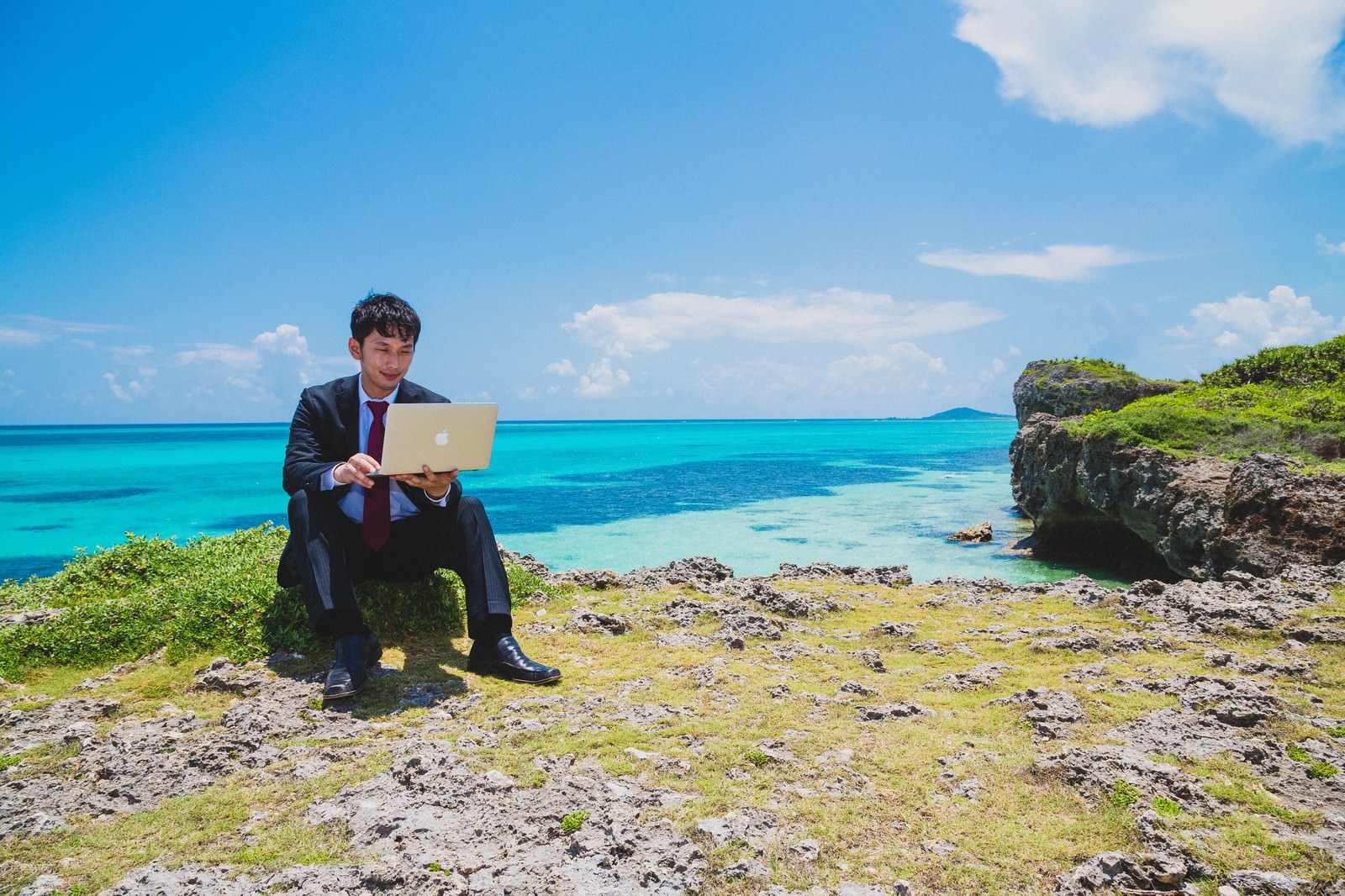 南国の海でスーツ姿でパソコン作業をする男性［モデル：大川竜弥］