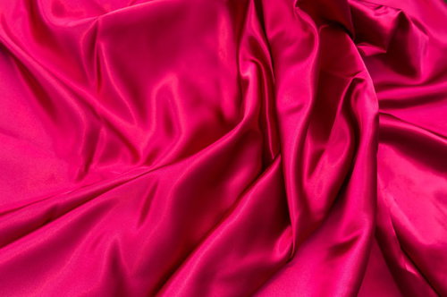 波打つように折り目が広がるピンク色のサテン生地