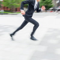 屋外の舗装道路を動きのブレで走るジャケットの人物の写真