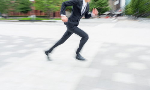 屋外の舗装道路を動きのブレで走るジャケットの人物