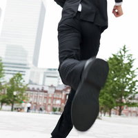 曇り空の屋外広場で片足が地面から離れて走るストライプスーツの人物の写真