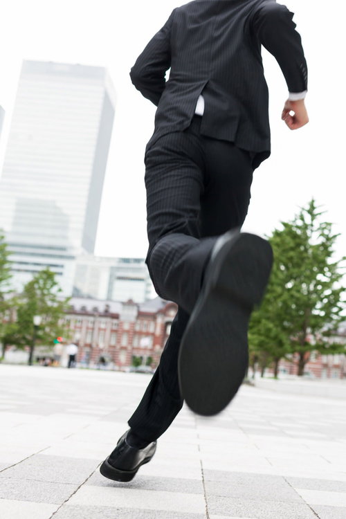曇り空の屋外広場で片足が地面から離れて走るストライプスーツの人物