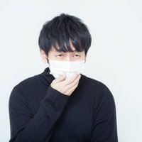 白いマスクを手で押さえる黒い長袖の黒髪の人物の写真