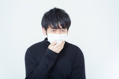白いマスクを手で押さえる黒い長袖の黒髪の人物
