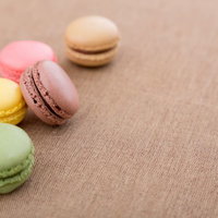 茶色い布の上に5個並んだパステルカラーのマカロンの写真