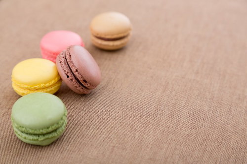 茶色い布の上に5個並んだパステルカラーのマカロン