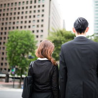 都会の交差点で信号待ちをするスーツ姿の男女の写真