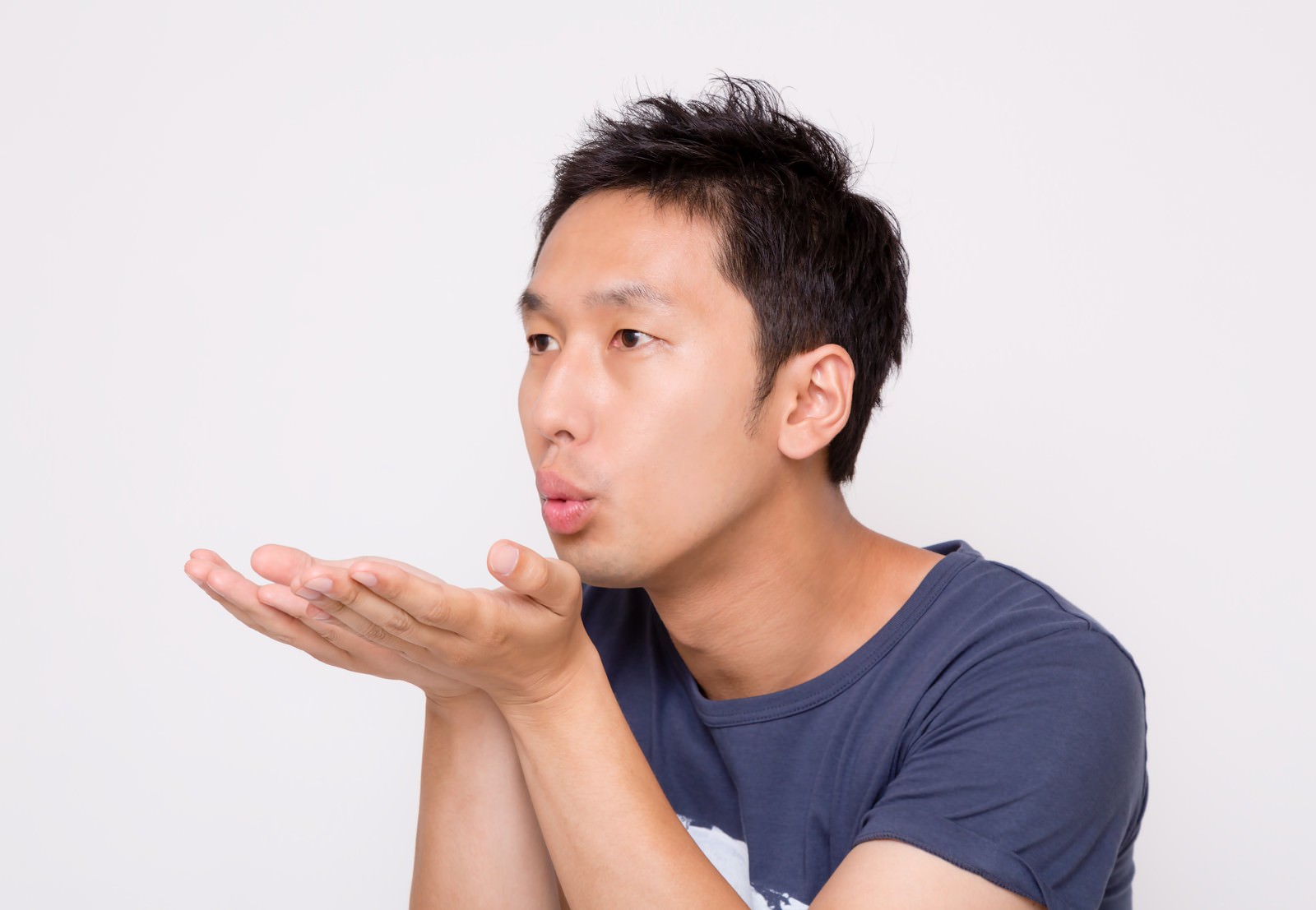 両手を合わせて息を吹く紺Tシャツの男性の横顔［モデル：大川竜弥］