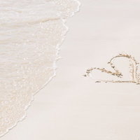 砂浜に描いたハート型の絵に白い波が打ち寄せる俯瞰写真の写真