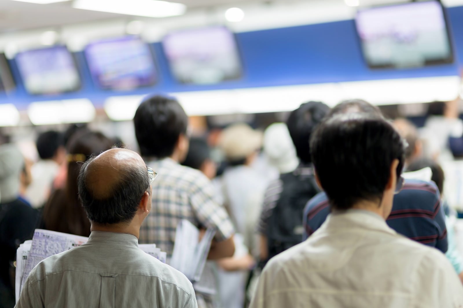 場外馬券場のモニターの前に立つ人々の後ろ姿