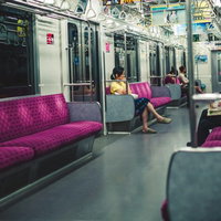 紫色のシートに乗客が座る夜間の電車車内の写真