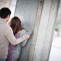 屋外のコンクリート塀で後ろ姿の茶色ニットの男性と花柄の女性の写真