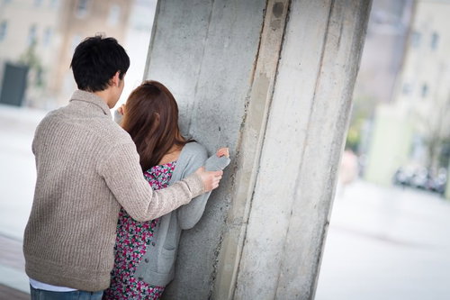 屋外のコンクリート塀で後ろ姿の茶色ニットの男性と花柄の女性