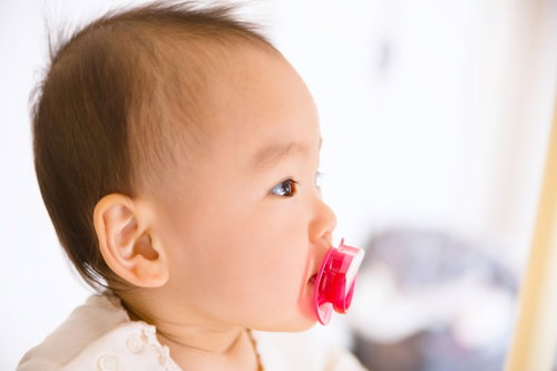 赤いおしゃぶりをくわえた赤ちゃんの横顔