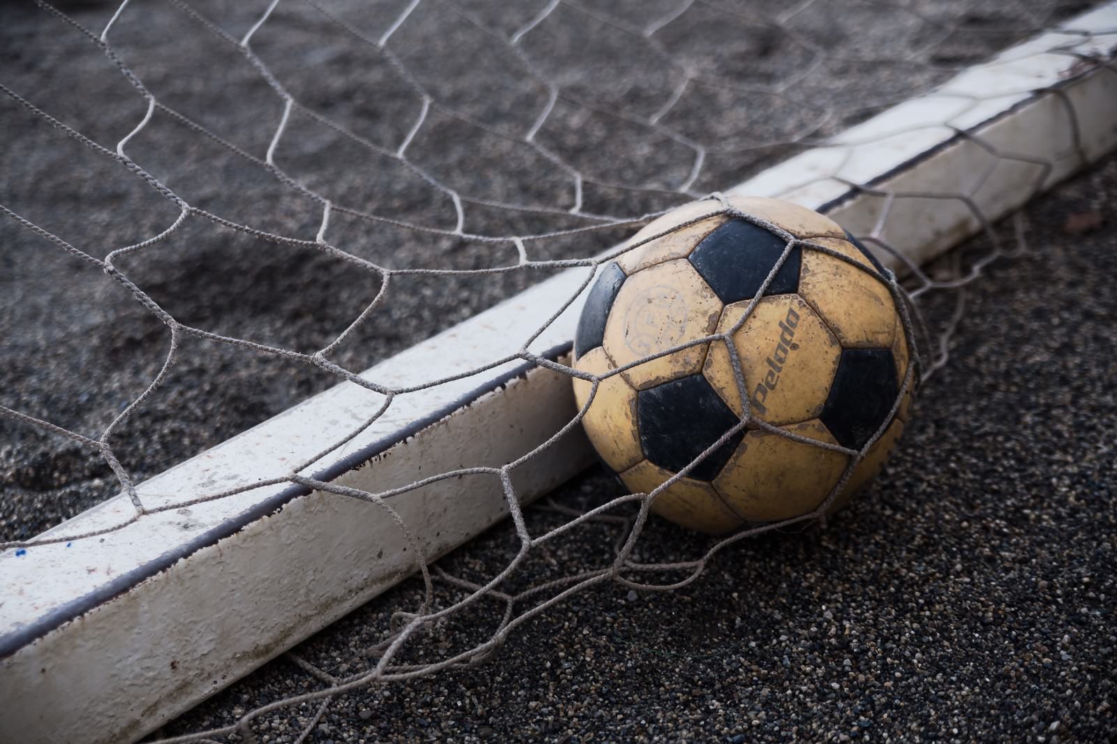 ゴールネットに接触した黒と黄土色のサッカーボール