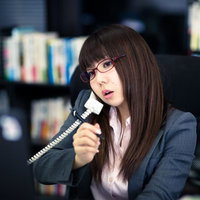 本棚の前で受話器を持つ眼鏡の女性の写真