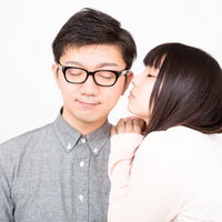 彼氏の耳元に顔を近づける長い髪の彼女の写真