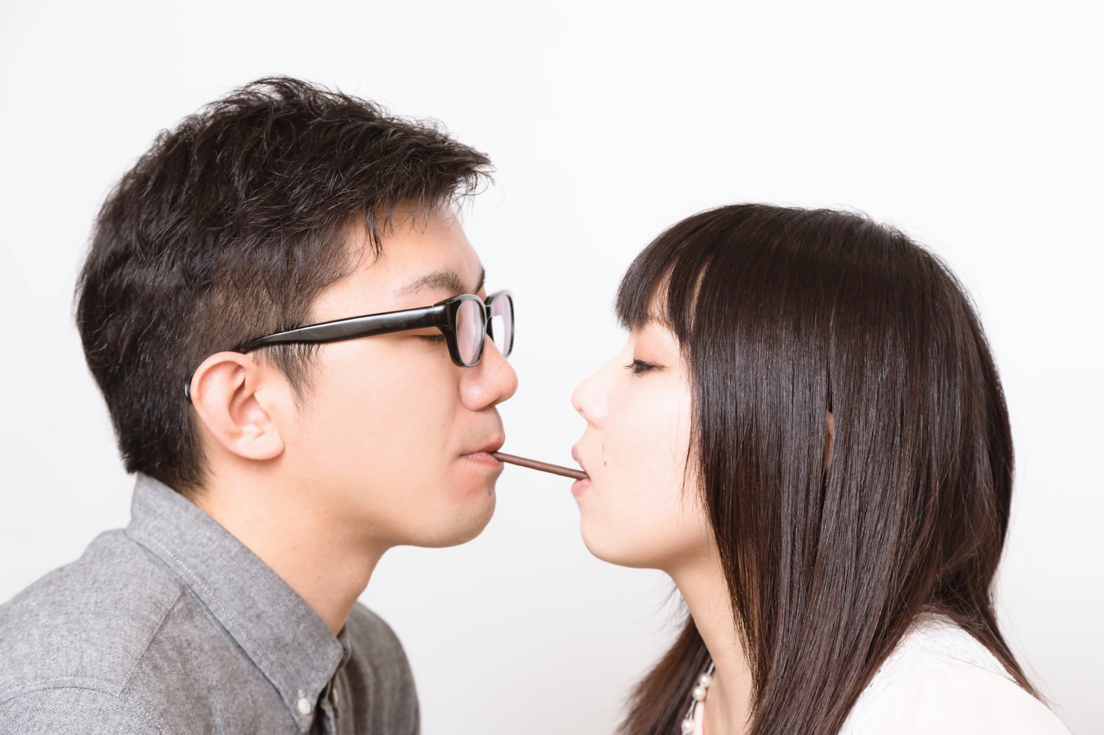 ポッキーを口にくわえて向き合うカップル［モデル：OZPA Lala］