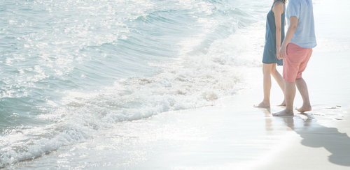 押し寄せる波に引き寄せられるカップルが浜辺で寄り添う